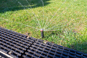 Sprinkler System in Action. A close-up of an active sprinkler head watering a lawn, with water jets...