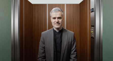 Portrait of a smiling priest standing in an elevator