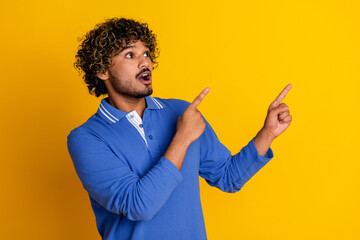 Young man in a blue polo shirt pointing with both hands against a vibrant yellow background,...