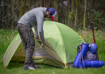 Man camping in nature, setting up the tent for overnight staying near forest river.