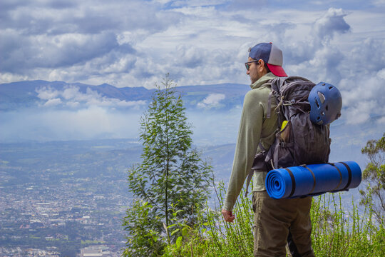 An adventurer in rugged outdoor gear stands on a hilltop, surveying a sweeping valley with distant peaks under a dramatic, cloudy sky. Ideal for adventure and exploration themes. - Powered by Adobe