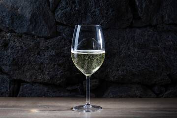 glass of cold champagne or sparkling white wine with sparkling bubbles on lava stones background