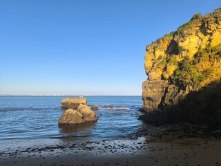 Rocks and their reflections glow in the warm light of the sunset, creating a stunning coastal scene.