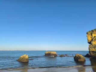 A lonely rock rests in calm waters, its form reflected in the stillness of the surrounding sea.