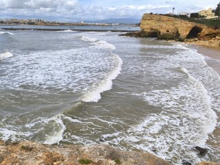 Soft foam forms over coastal stones as waves gently roll in, creating a peaceful, calming beach scene.