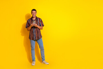 Young fashionable man using smartphone on yellow background, showcasing modern lifestyle,...