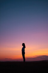 young woman stands gazing into vast skyline her silhouette outlined by sunrise that paints sky with vibrant hues symbolizing