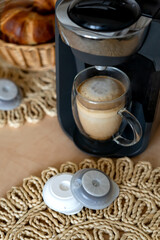 A glass of latte with foam in a capsule coffee maker. Black small coffee maker for daily drink for apartment and office.