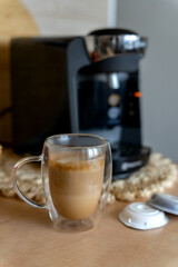 Cup of latte with foam and capsules for brewing coffee on the background of capsule coffee maker in home kitchen.