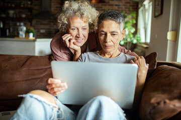 Senior lesbian couple using laptop on cozy couch at home