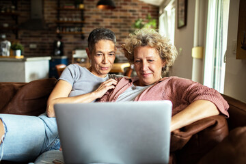 Senior lesbian couple using laptop on cozy couch at home