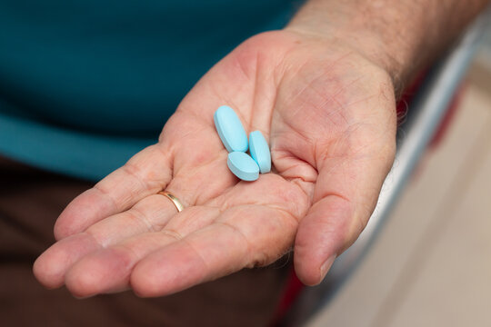 Mão de um homem idoso com três comprimidos de viagra.