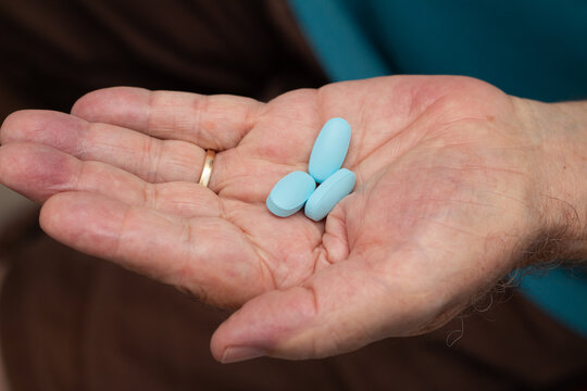 Mão de um homem idoso com três comprimidos de viagra.