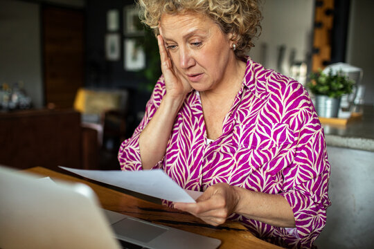 Worried senior woman reading bills at home