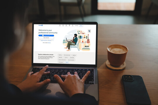 Bangkok, Thailand. April 16, 2025; Hands typing on MacBook Pro displaying LinkedIn login page with coffee on wooden table in cafe.