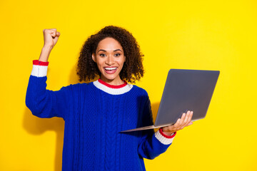 Excited young woman with afro hairstyle holding a laptop while celebrating success against a...
