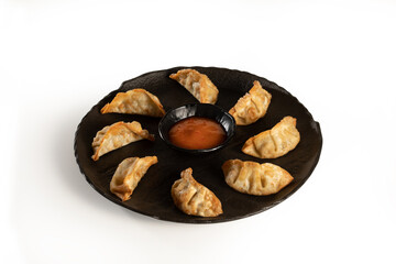Tasty gyoza served in a black plate with Teriyaki sauce on white background, stock
