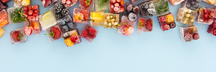 Blue background with ice cubes with frozen berries and fruits and mint, banner