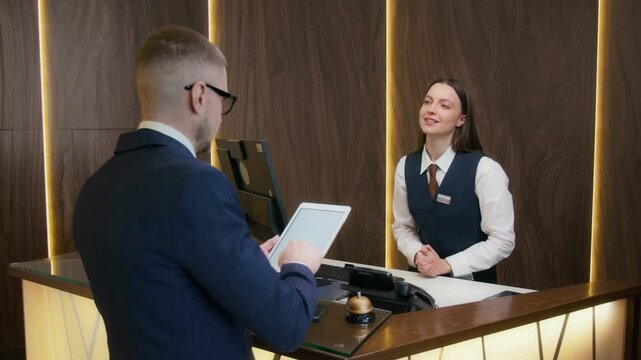 Smiling female receptionist asking male guest to sign on digital tablet while completing check-in process at front desk of upscale hotel