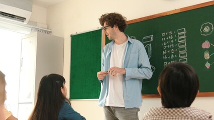 Professional mentor looking around classroom while standing in front of blackboard with math formula or theory. Diverse elementary student learning or studying and sitting in Math lesson. Pedagogy.