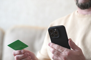 Man using smartphone and green credit card for online shopping