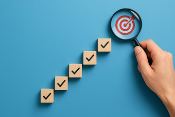 Hand holding magnifying glass over checklist cubes revealing a target icon on blue background.