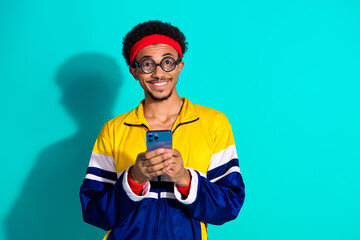 Energetic male with retro vintage sportswear holding smartphone against teal background, expressing...