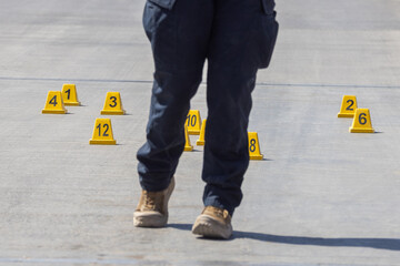 	Law enforcement officer walking through a crime scene surrounded by evidence markers.