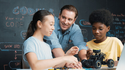 Caucasian teacher looking at laptop screen while explain car model system at blackboard with coding...