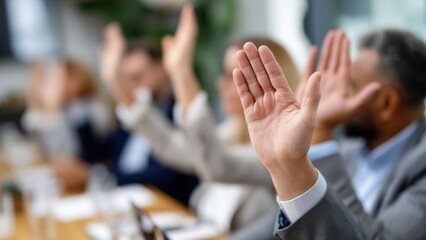 A group of professionals in suits raise their hands in unison during a meeting to show agreement on a decision, during a voting session.