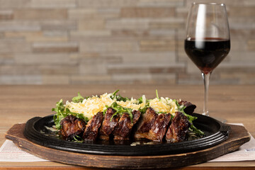 grilled meat with parmesan and rocket on a hot plate with a red glass wine, wooden table and wall...