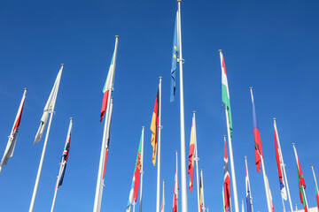 A bright blue sky with a few scattered clouds stretches above. Tall flagpoles stand still, their...