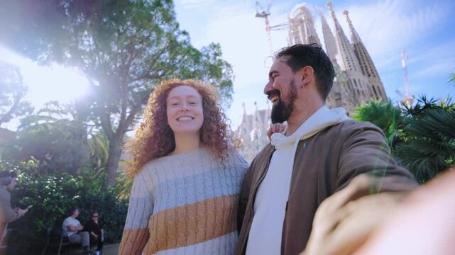 Young caucasian couple on a video call talking to the camera in front of the sagrada familia, enjoying their vacation together.