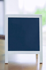 Blank vertical chalkboard on wooden table with white frame, ideal for creative mockups, menu boards or announcements.
