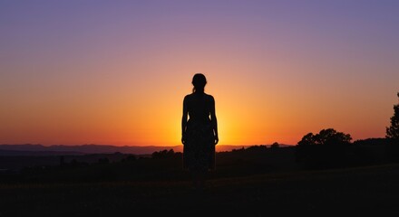 Obraz premium Woman Silhouette at Sunset Hilltop - A woman stands silhouetted against a vibrant sunset, symbolizing peace, hope, solitude, contemplation, and new beginnings
