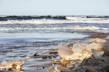 
a wavy sea and a sandy beach partially covered with ice chunks.