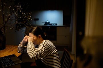 a tired woman working at home in the kitchen at the computer in the middle of the night
