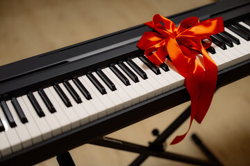 A digital piano with a red ribbon tied around it, suggesting it is a gift. © Ananass