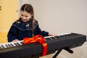A young girl excitedly opens a gift-wrapped keyboard with a red ribbon.