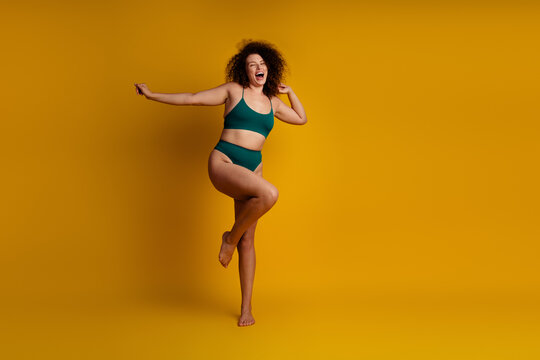 Confident young woman with curly hair showing self acceptance and positive energy against a vibrant yellow background