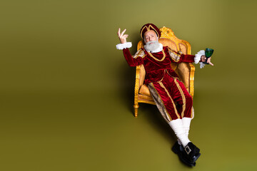 Nobleman in a Historical Costume Sitting Elegantly in a Classic Chair Against a Khaki Background
