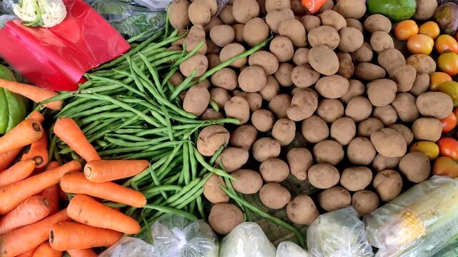 A variety of fresh vegetables, including potatoes, carrots, green beans, tomatoes, chayote and corn. Displayed at a market stall