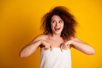 Confident young woman with curly hair wrapped in a towel smiling against a yellow background,...