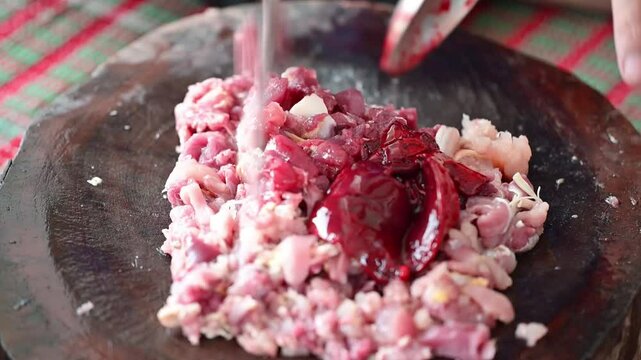 Mincing chicken meat on cutting board for northern thai style spicy minced chicken meat salad call Larb Kai Muang.