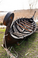 A meticulously crafted wooden Viking longship rests on the grass near a lake, showcasing intricate...