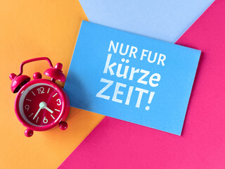 Red alarm clock and blue card with text NUR FÜR KURZE ZEIT! meaning ONLY FOR A SHORT TIME! in German on colorful background