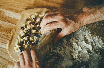 Close-up of hands wrapped in a Pain aux raisins roll with raisins on a wooden surface