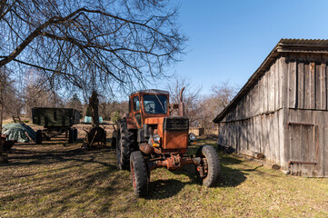 Naklejka premium Vintage tractor parked near an old barn under clear blue sky during daytime