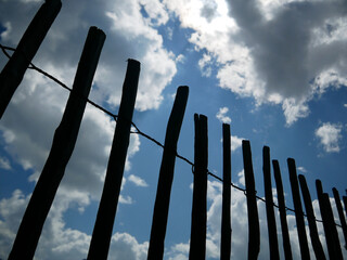 enclosure of thin wooden fence with bright blue cloudy sky in background