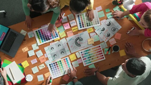 Top down view of designer compare color palettes with laptop and design product. Aerial view of marketing team working together to choose color while discussing about logo graphic design. Symposium.